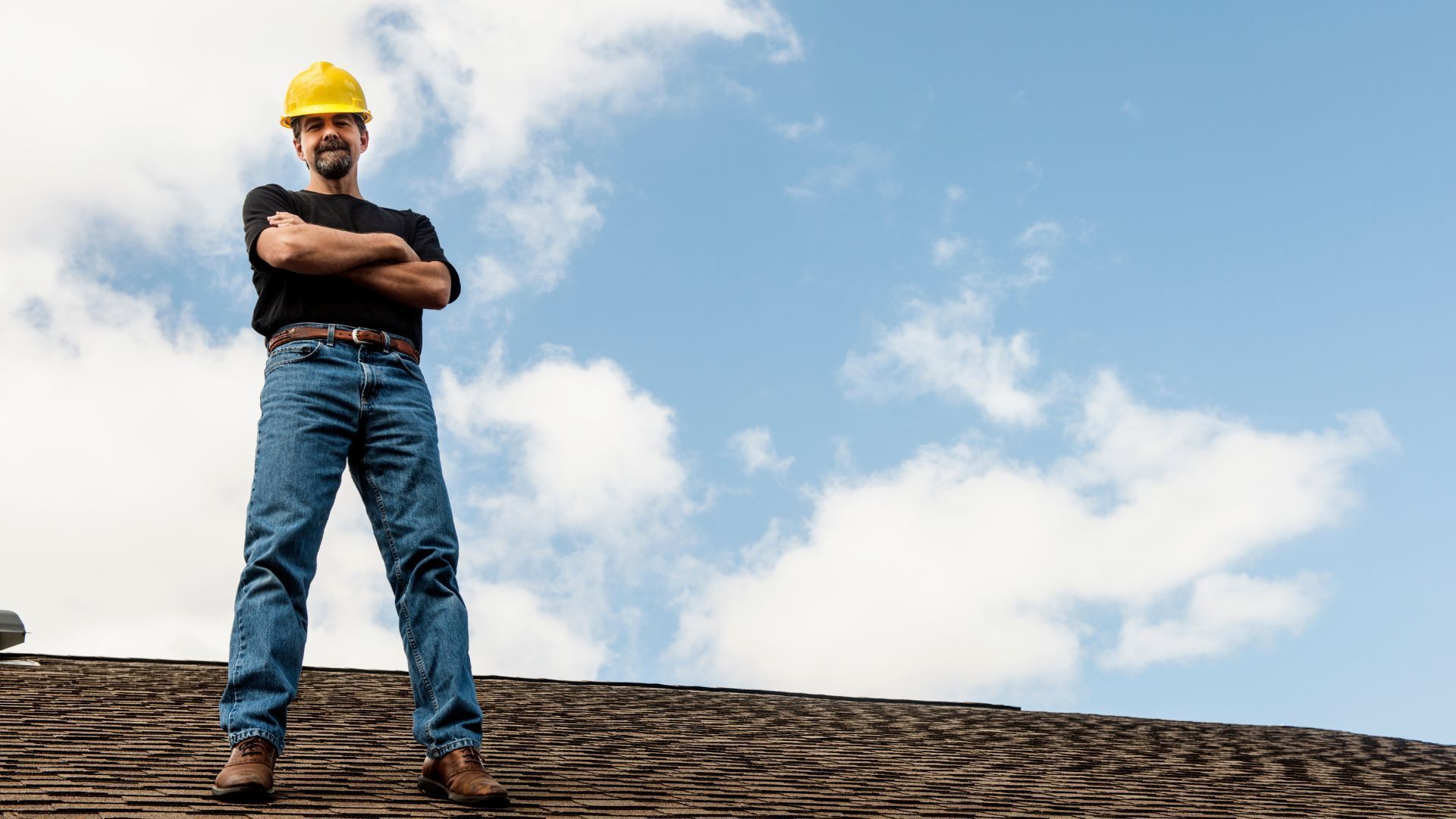 A man wearing a hard hat is standing on top of a roof.