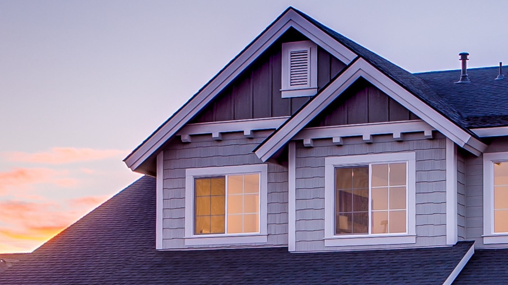 A house with a black roof and a sunset in the background.