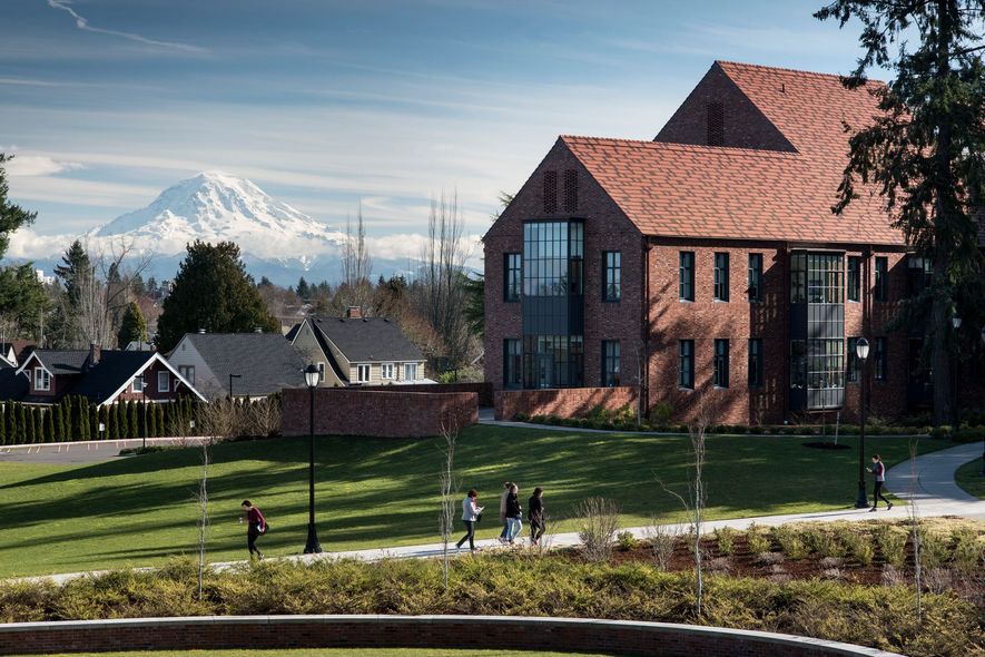 Red-roofed brick house in a green field with people walking, snowy mountain in the distance