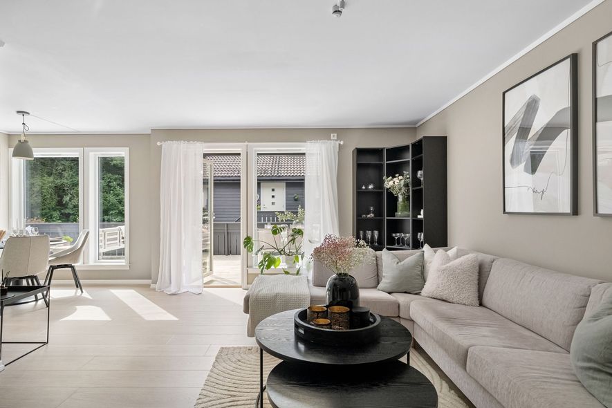 Bright living room with beige sectional, round black coffee table, and sliding glass doors to a balcony.