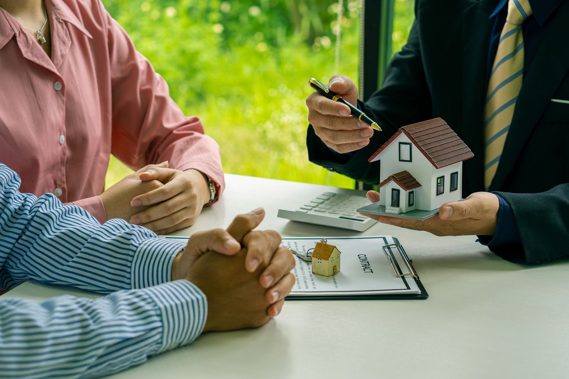 People meeting over a house model and documents at a table, discussing a home purchase