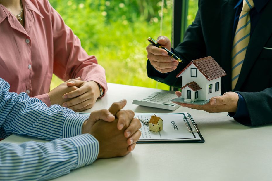 People meeting over a house model and documents at a table, discussing a home purchase