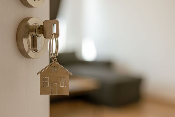 Key in a door lock with a house-shaped keychain, blurred apartment interior in the background