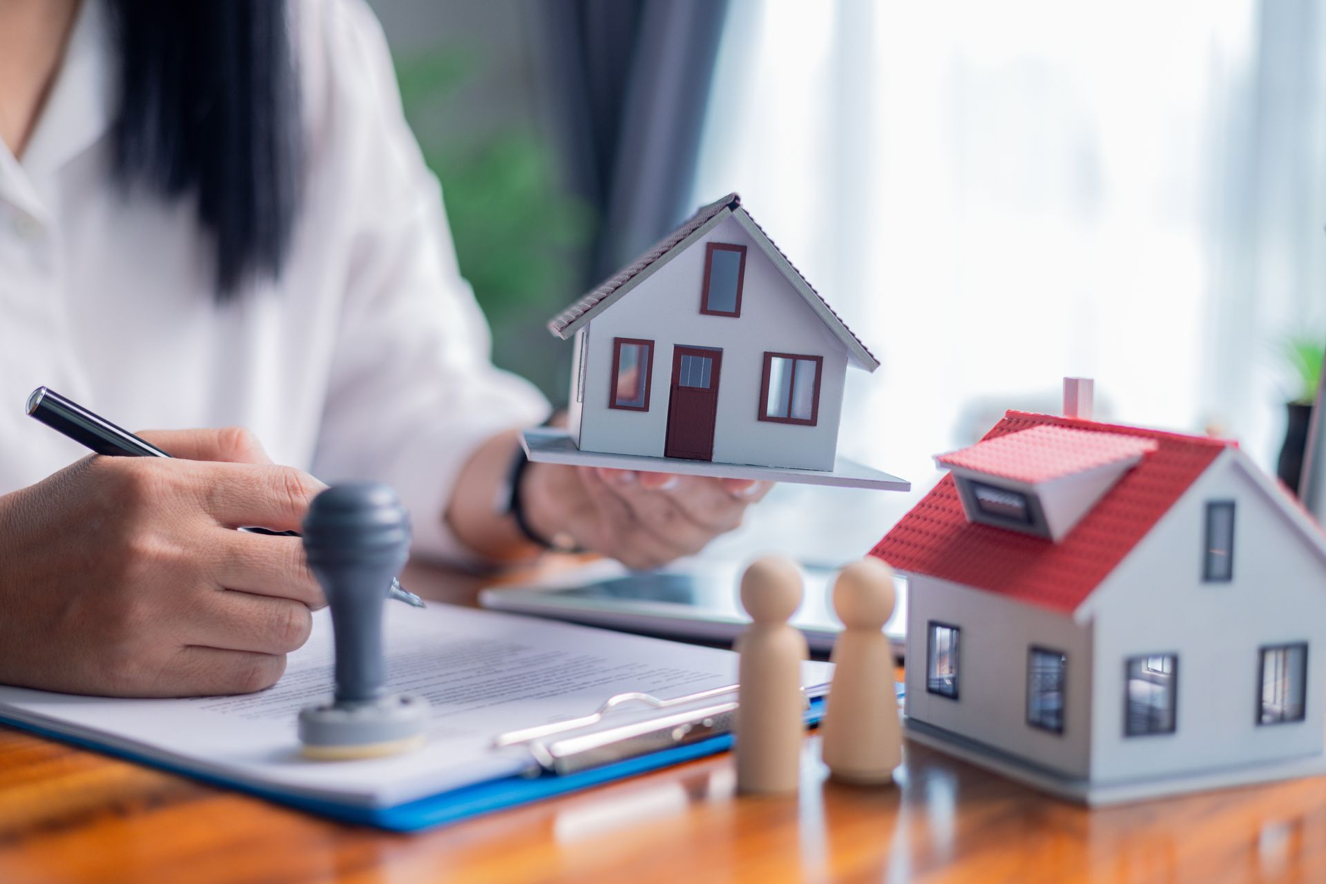 Hand signing house papers beside model homes and a stamp on a desk