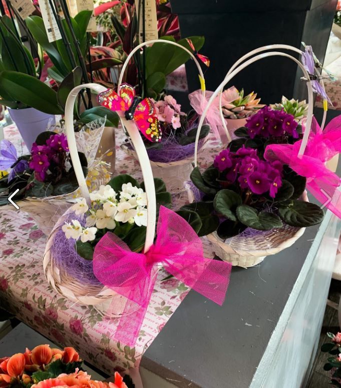 Cesti di fiori con fiocchi rosa e fiori viola, bianchi e rosa su un tavolo.