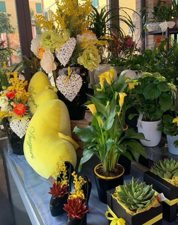 Esposizione di un negozio di fiori con palloncini a forma di cuore gialli, piante in vaso assortite e composizioni floreali.