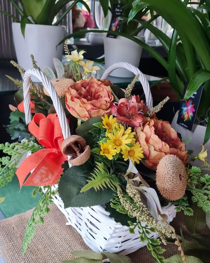 Cesto bianco di fiori misti con fiori arancioni, gialli e rossi su un tavolo
