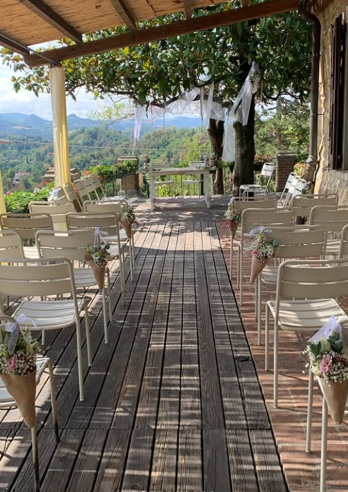 Percorso nuziale all'aperto con sedie bianche, vasi di fiori e vista sulle montagne sotto un pergolato di legno.