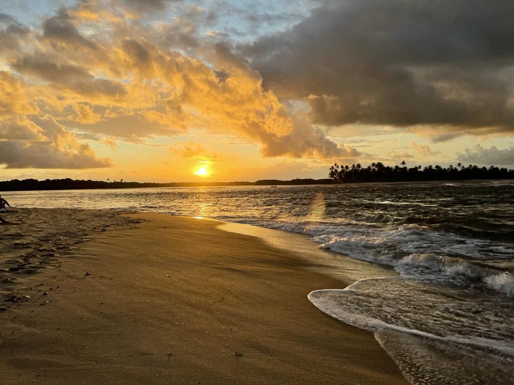 Pôr do sol sobre uma praia de areia com ondas e reflexo dramático das nuvens