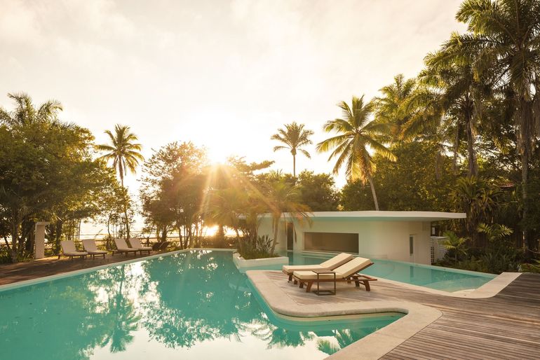 Piscina de resort tropical com espreguiçadeiras, palmeiras e a luz quente do pôr do sol.