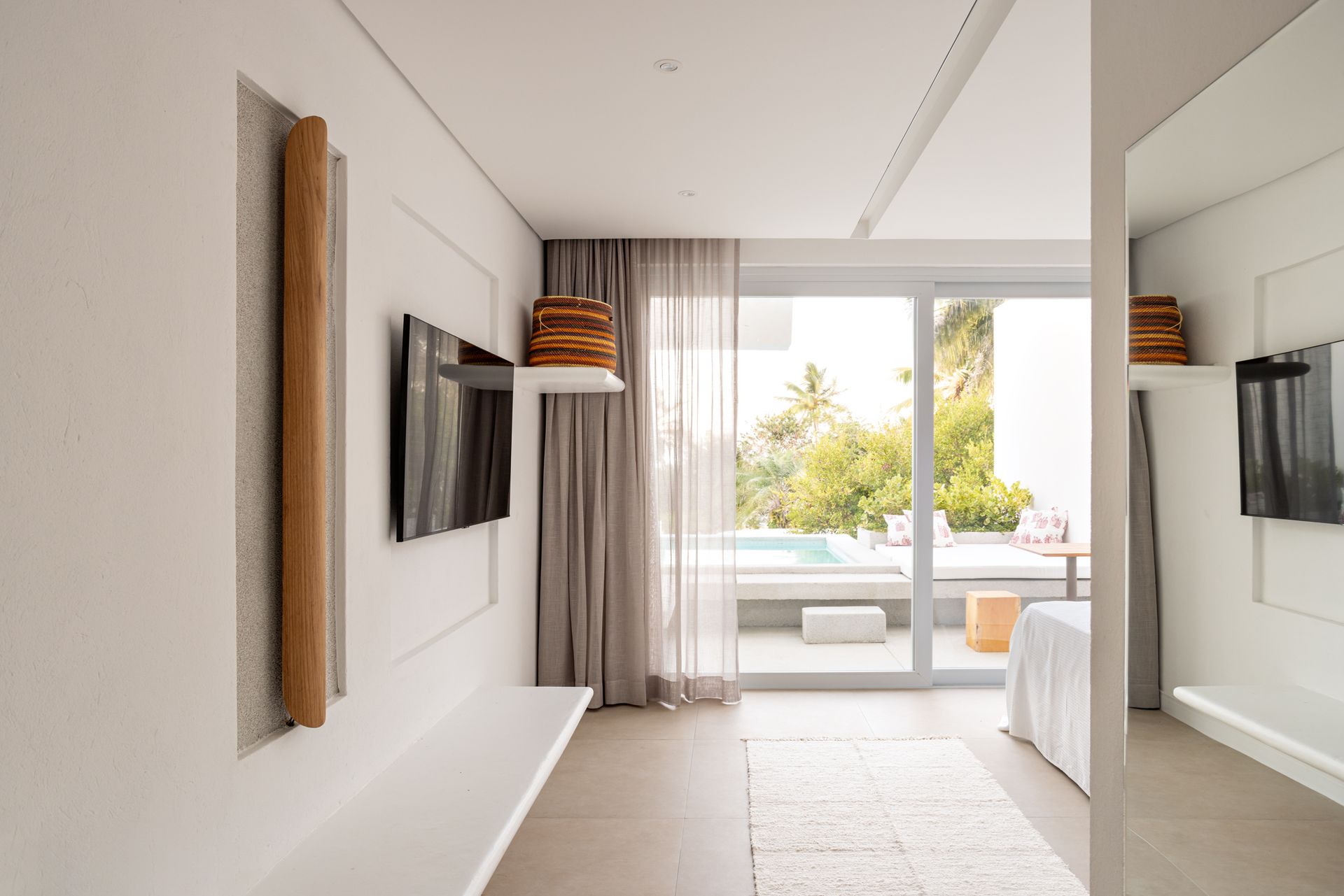 Quarto moderno e minimalista com TV de parede, cortinas do chão ao teto e uma varanda iluminada com vista para o jardim.