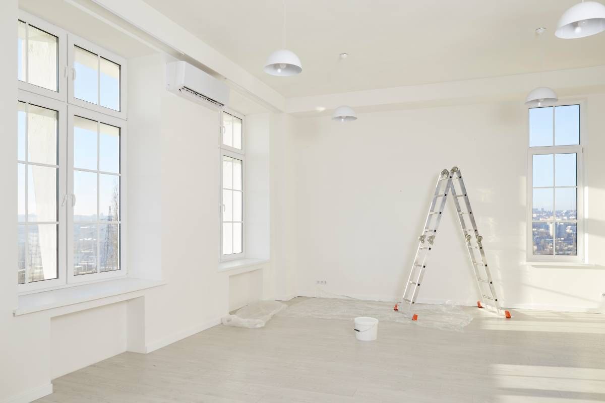 Interior of a spacious renovated apartment with ladder, paint can, fresh white walls, and large windows at Mountain Paint & Decorating near Arden, NC