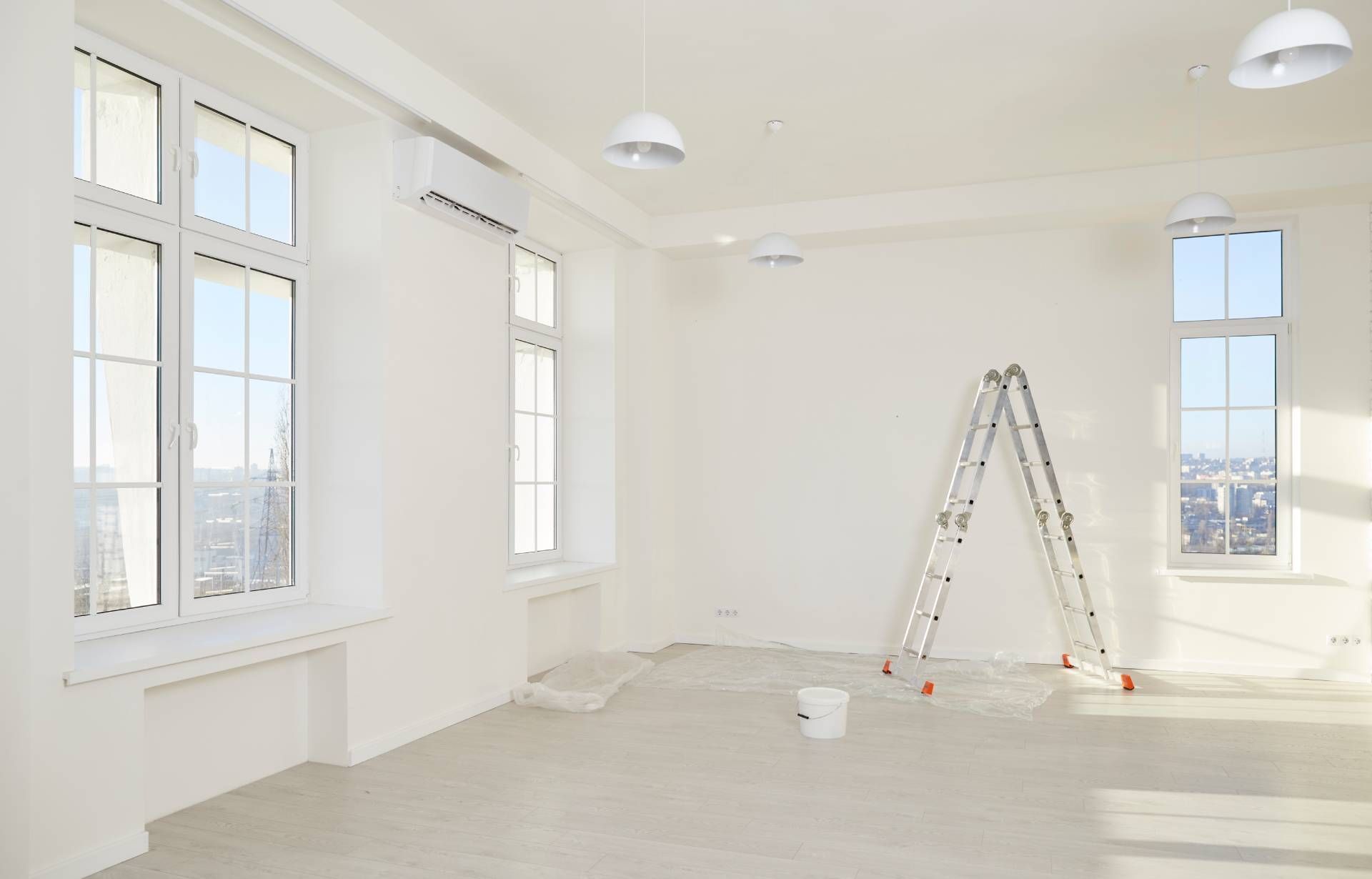 Interior of a spacious renovated apartment with ladder, paint can, fresh white walls, and large wind