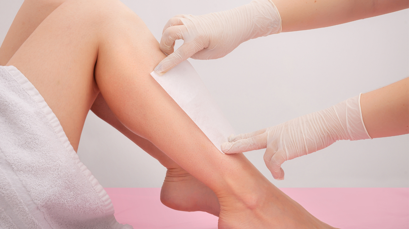 Person applying lotion to smooth, shaved legs against a pink background.