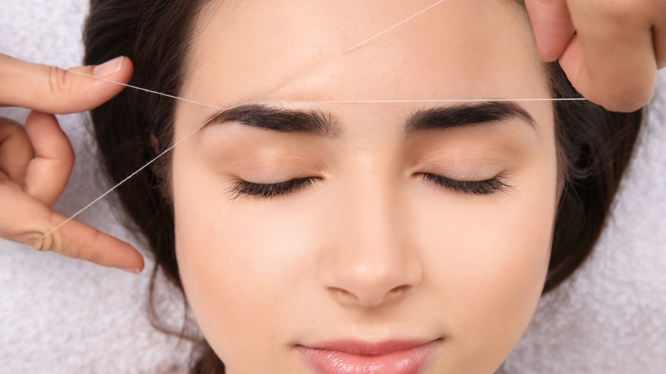 Threading eyebrow hair with a white thread on a closed eye