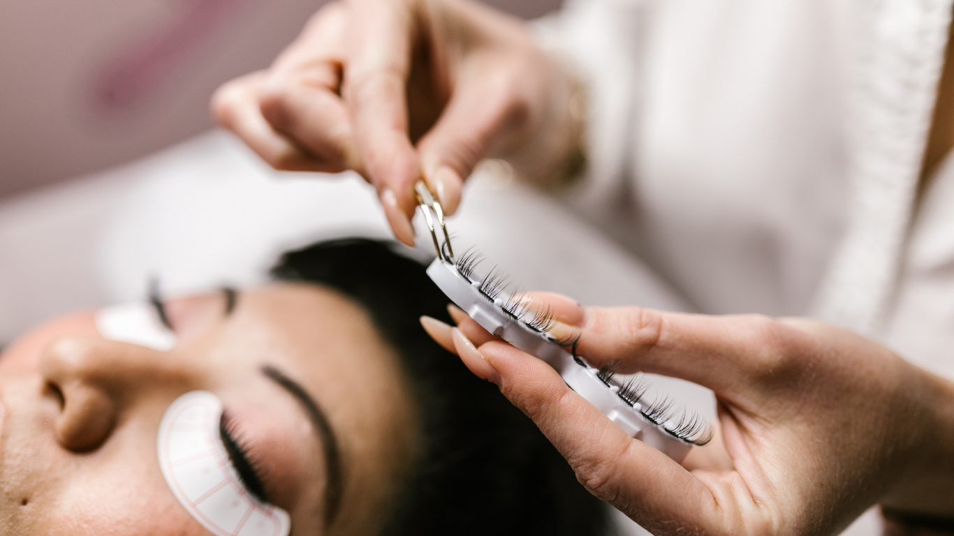 Person applying turquoise eye shadow with a brush to a client’s closed eyelid