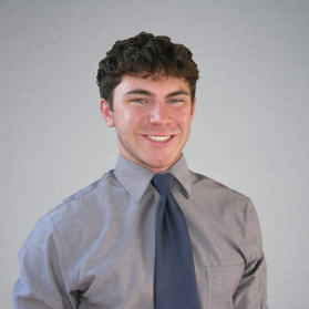 A man in a grey shirt and blue tie smiles for the camera