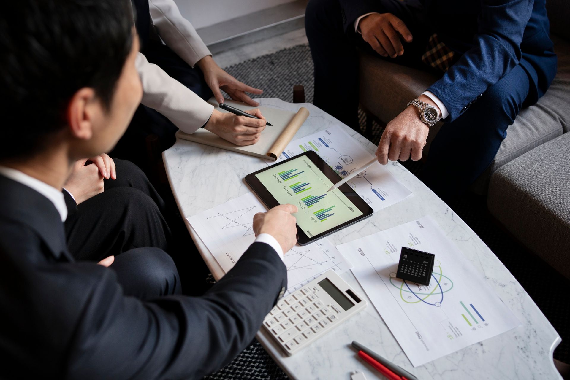 A group of people are sitting around a table looking at a tablet.