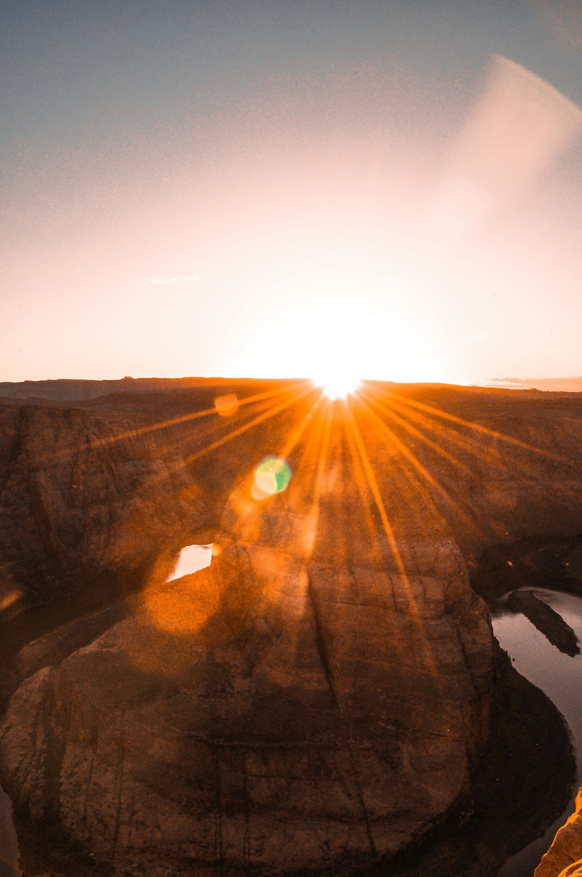 The sun is setting over a canyon with a river in the foreground.