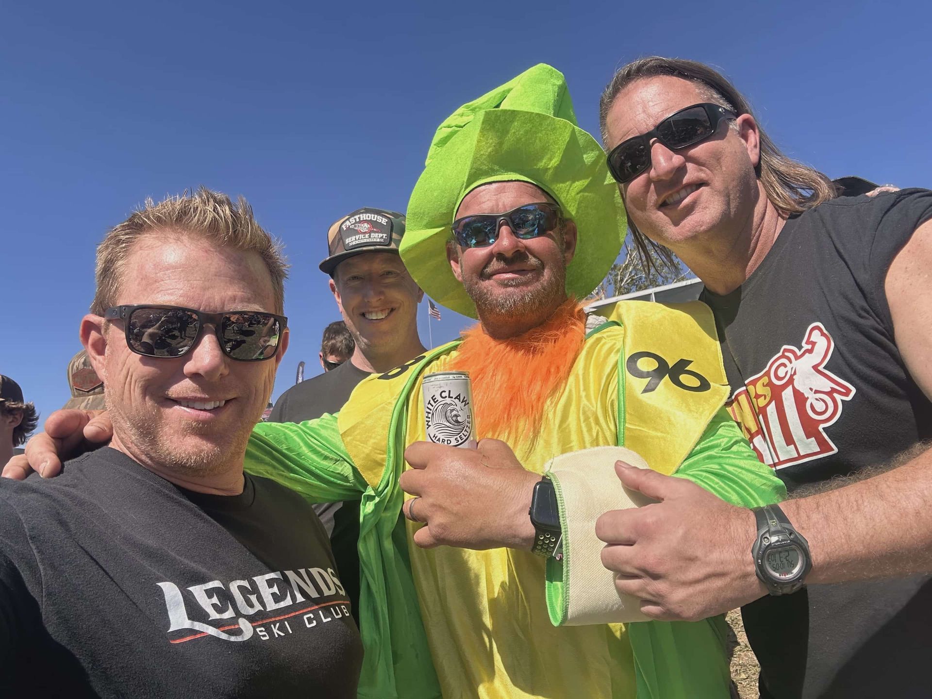 Four men posing for a selfie; one in a leprechaun costume with a beer and athletic tape.