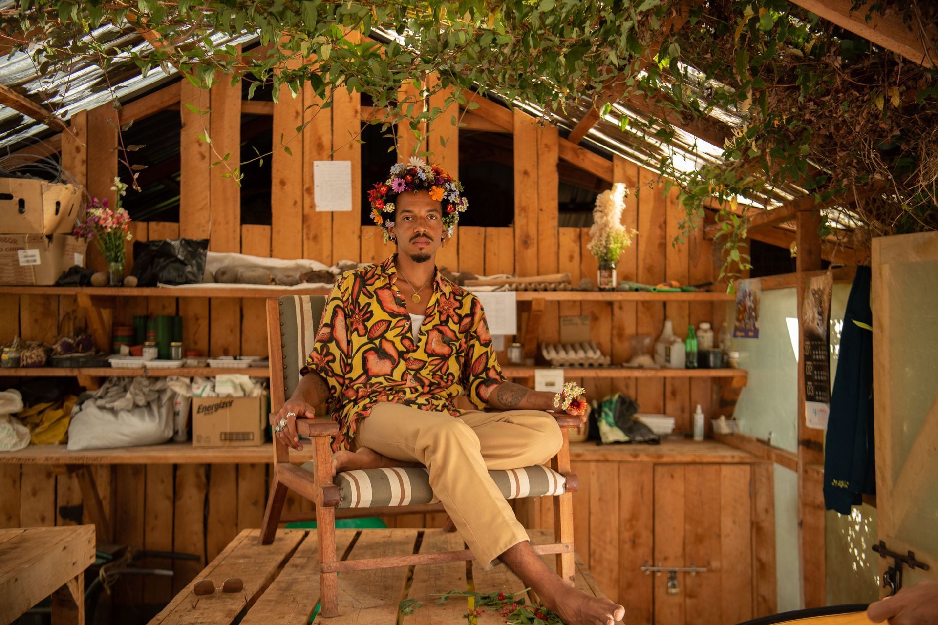 Person seated in a wooden market stall, surrounded by greenery and rustic shelves of goods.