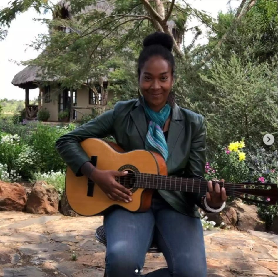 Person sitting outdoors with an acoustic guitar, smiling in a garden setting.