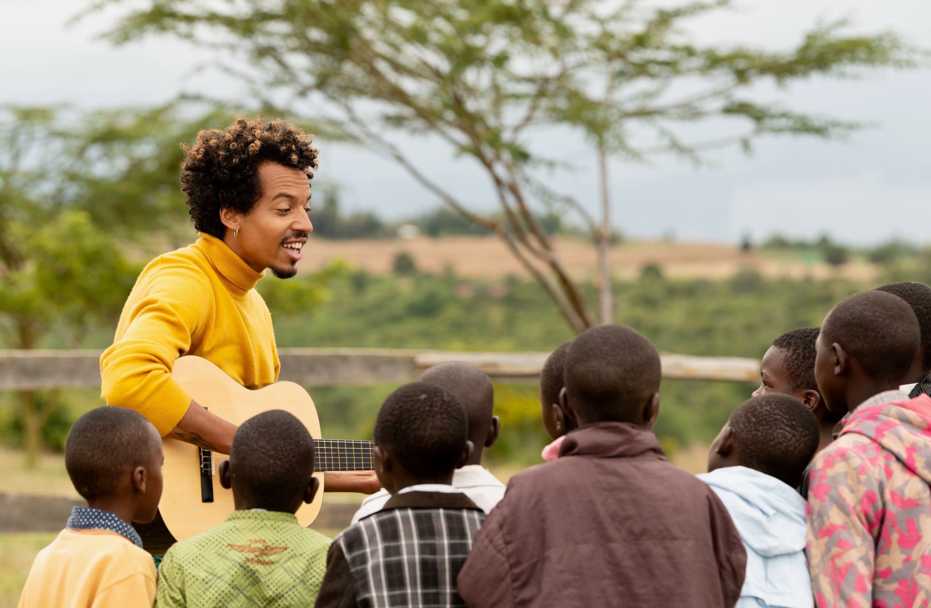 Woman playing guitar outdoors with a group of children listening in a field