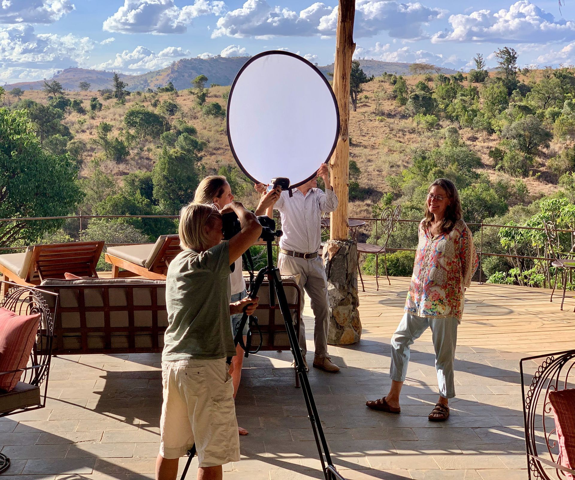 People setting up a large oval reflector on a tripod on a sunny patio with desert hills in the background