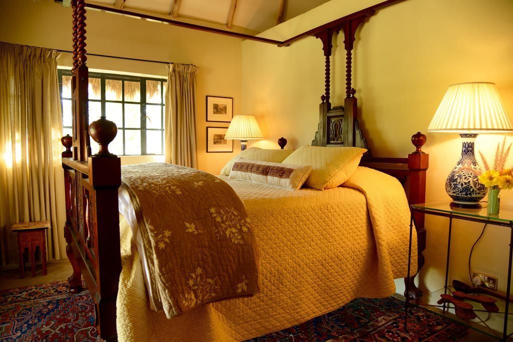 Warm bedroom with a four-poster bed, bedside lamps, and a window with curtains.