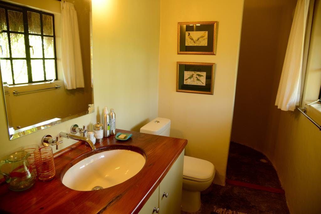Small bathroom with a wooden vanity, oval sink, toilet, mirror, and two framed pictures on beige walls.