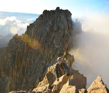 Climber on rocky mountain ridge above clouds at sunrise