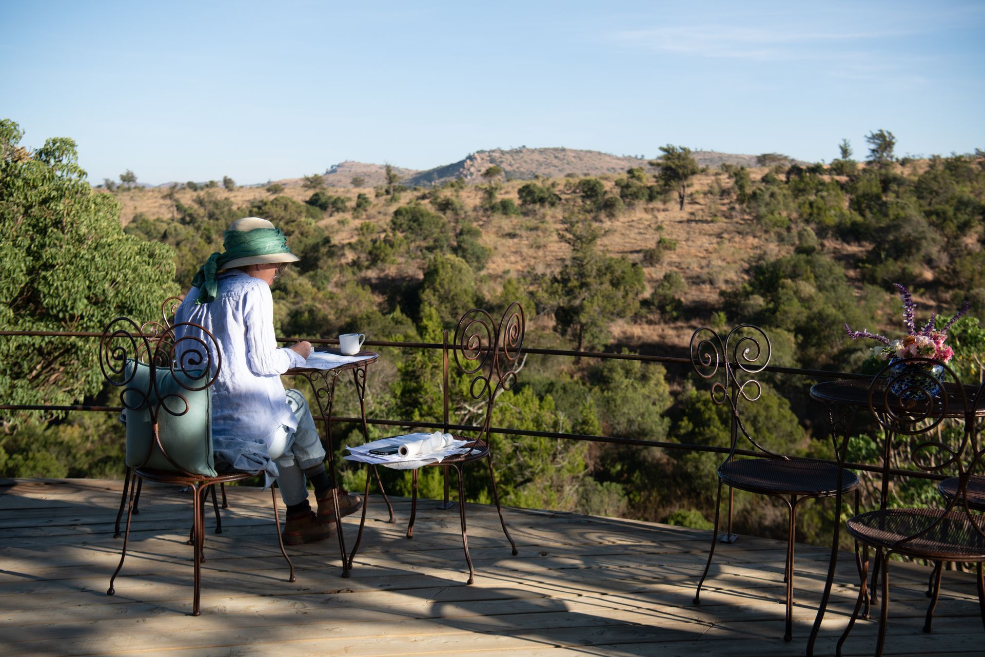 Person in a green hat sitting on a patio with a scenic desert hillside view