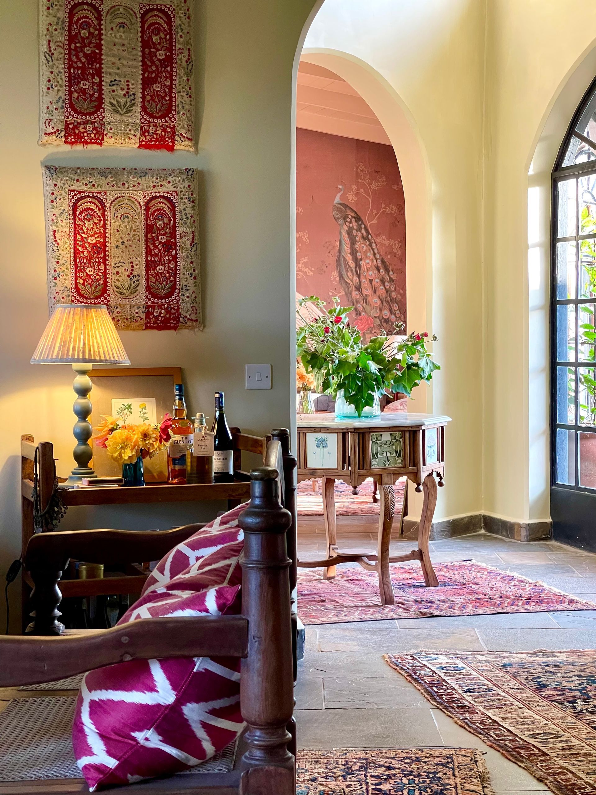 Bright living room with an arched doorway, colorful rug, lamp, and flowers on a small table