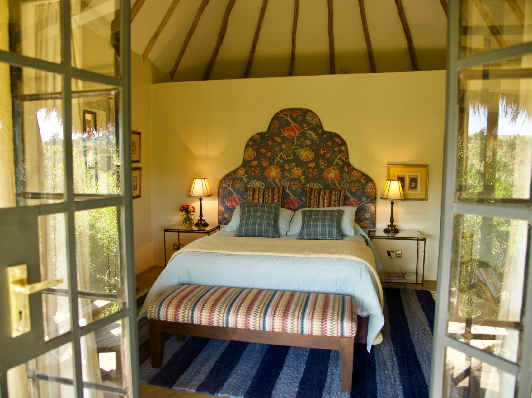 Cozy bedroom with canopy bed, floral headboard, open French doors, and striped rug