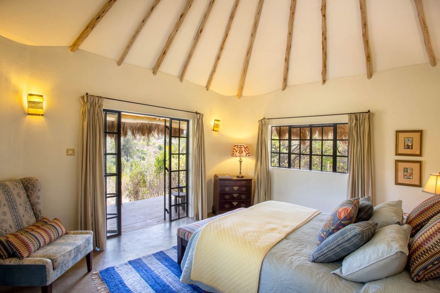Bright bedroom with vaulted ceiling, two couches, bed, and open doors to a sunlit patio.