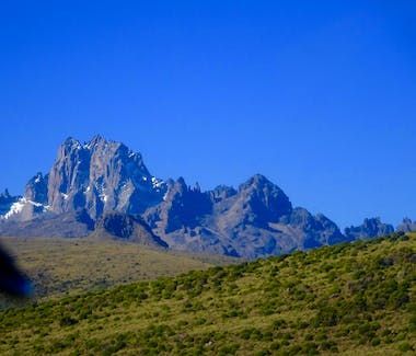 Rocky mountain peaks above a green hillside under a clear blue sky