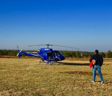 Blue helicopter on a grassy field with one person standing nearby under a clear sky