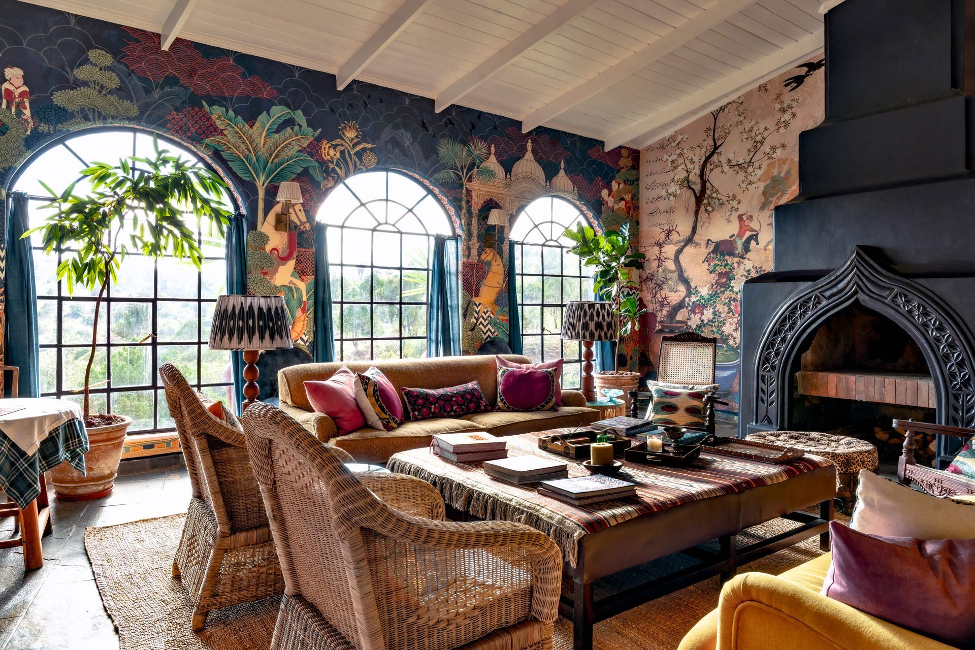 Cozy living room with arched windows, wicker furniture, patterned walls, and a large stone fireplace