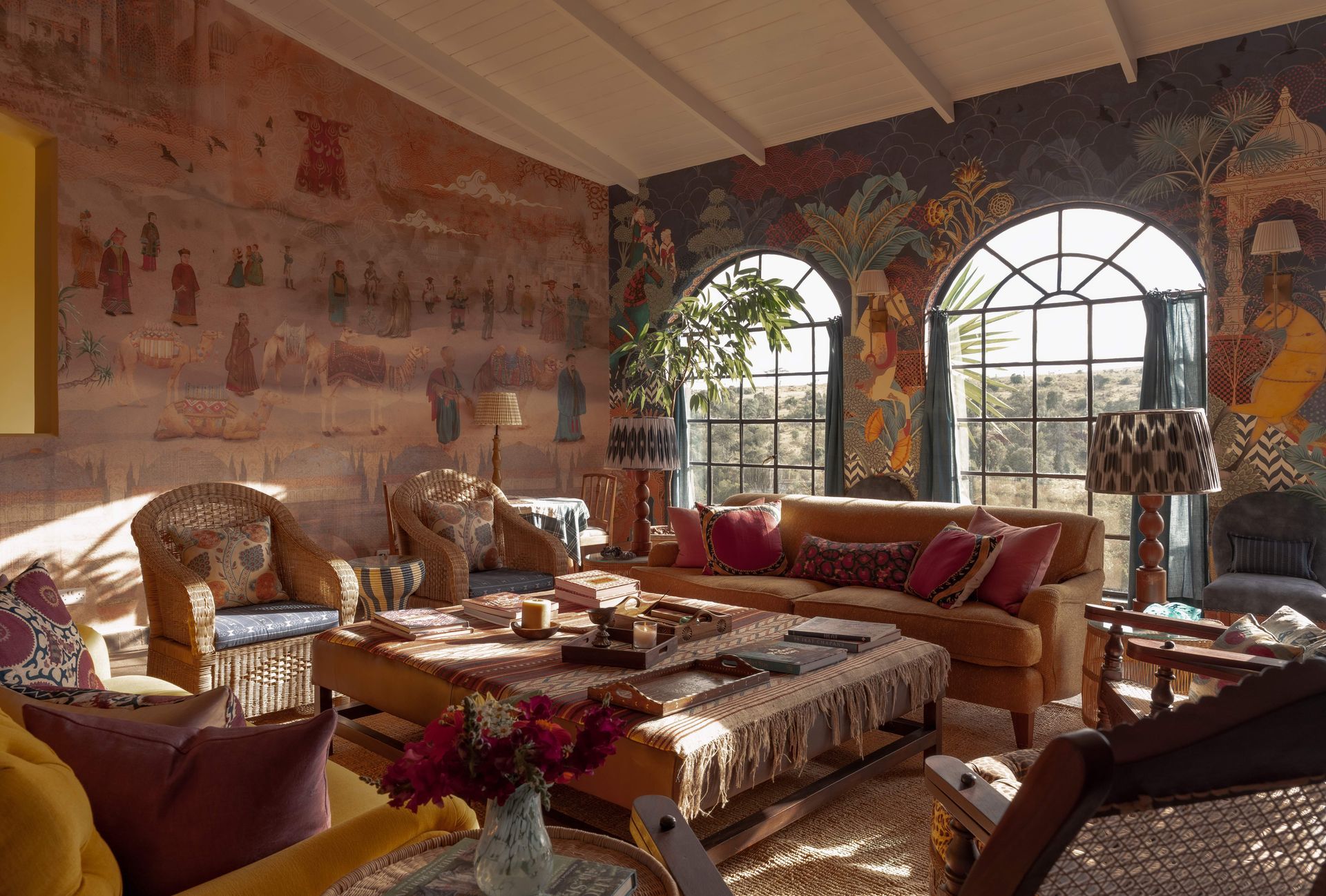 Sunlit living room with patterned sofas, a low table, and arched windows overlooking greenery