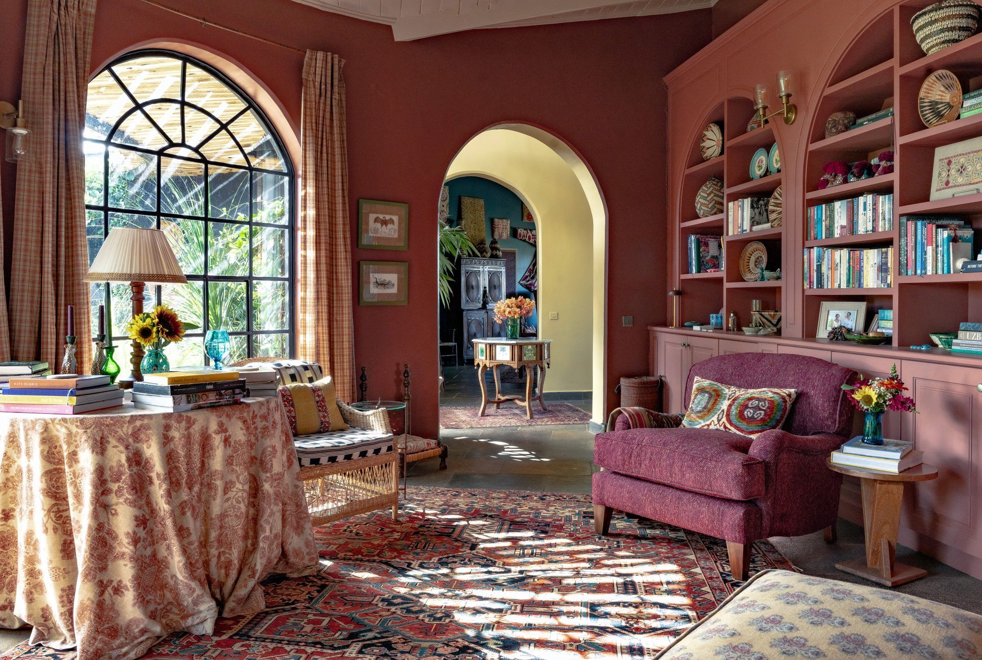 Cozy living room with arched window, patterned rug, purple chair, and shelves of books and decor