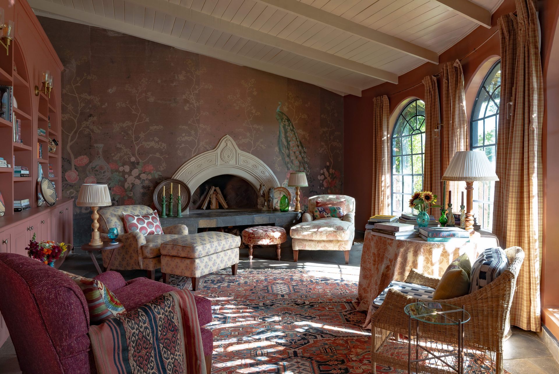 Elegant living room with a large fireplace, tall windows, ornate rug, and cozy seating in warm sunlight
