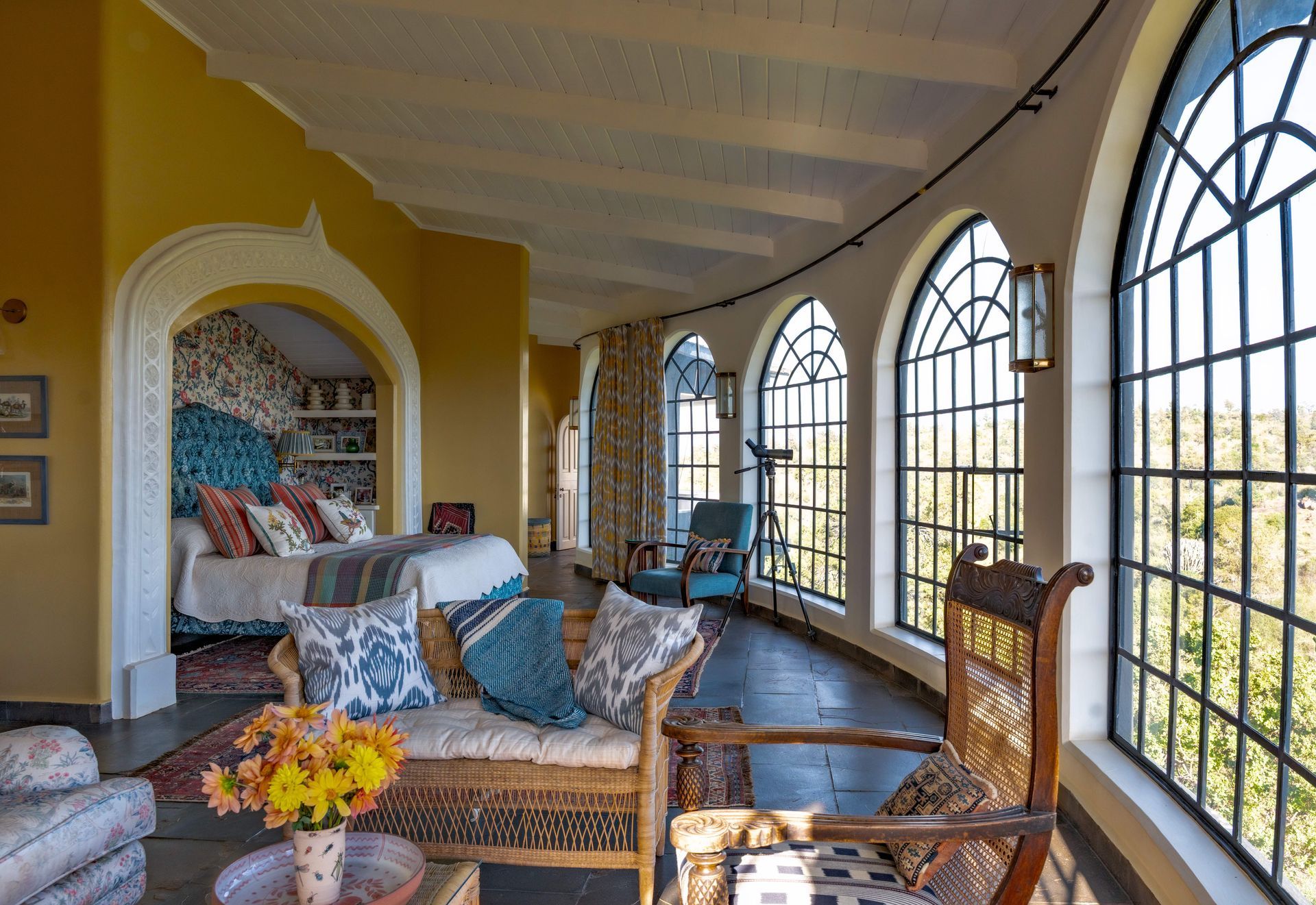 Sunlit room with arched windows, yellow walls, and patterned chairs beside a built-in bed nook.