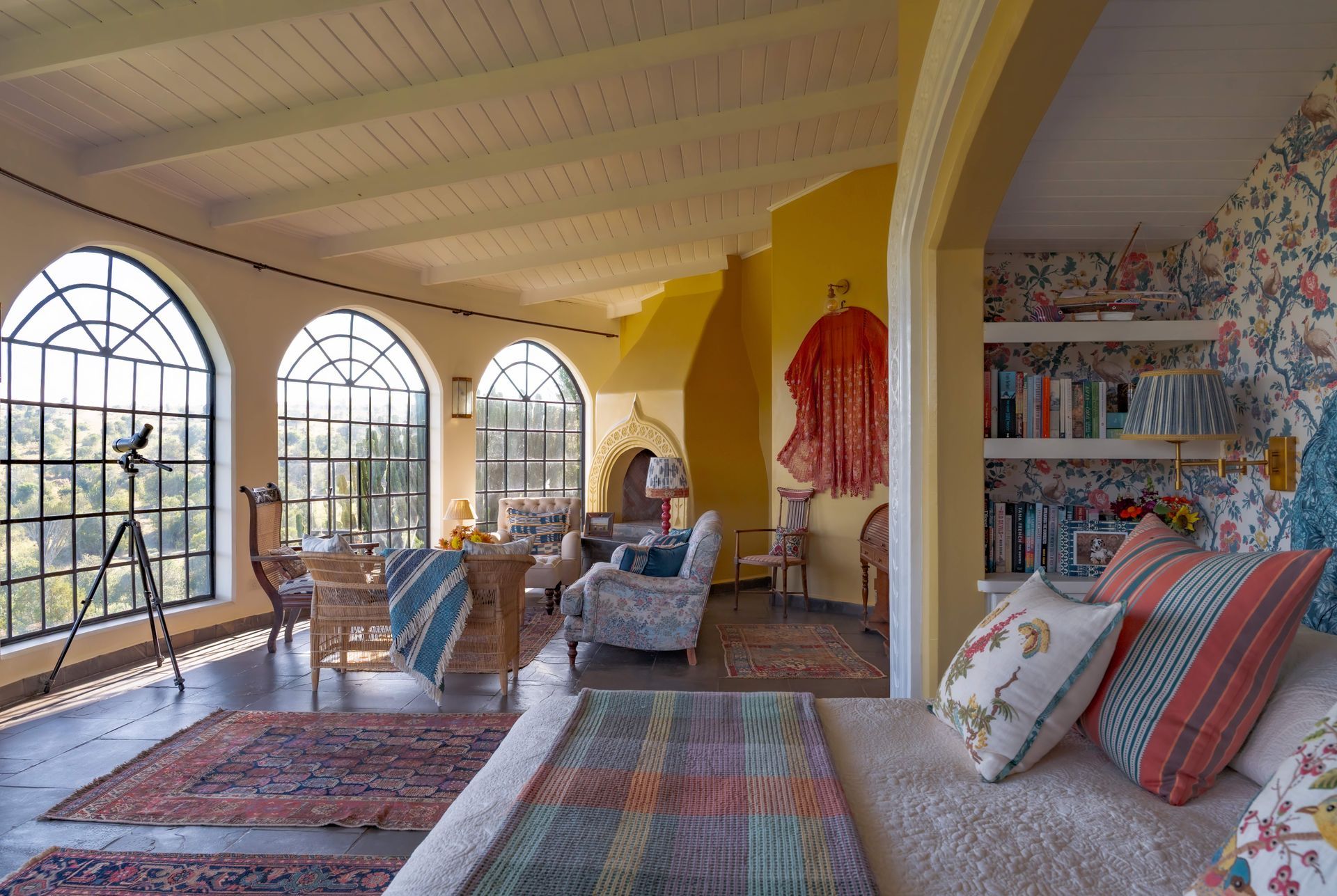 Bright sunlit living room with arched windows, colorful rugs, patterned pillows, and bookshelves.