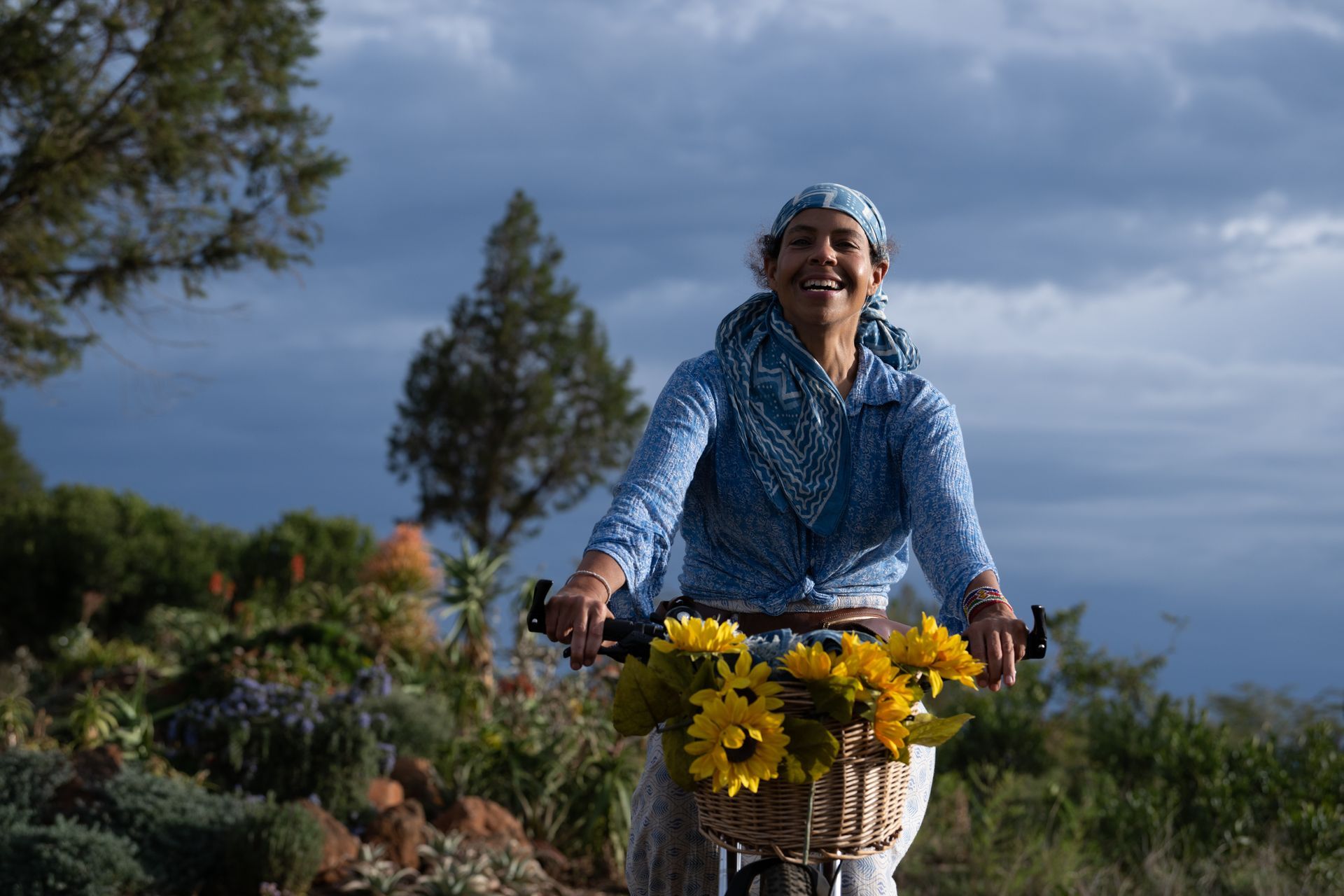 Cyclist smiling on a flower-decorated bike riding outdoors under a cloudy sky