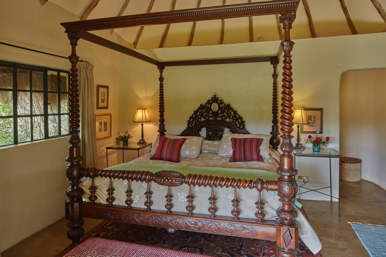 Ornate four-poster bed in a warm, sunlit bedroom with patterned pillows and carved wood details