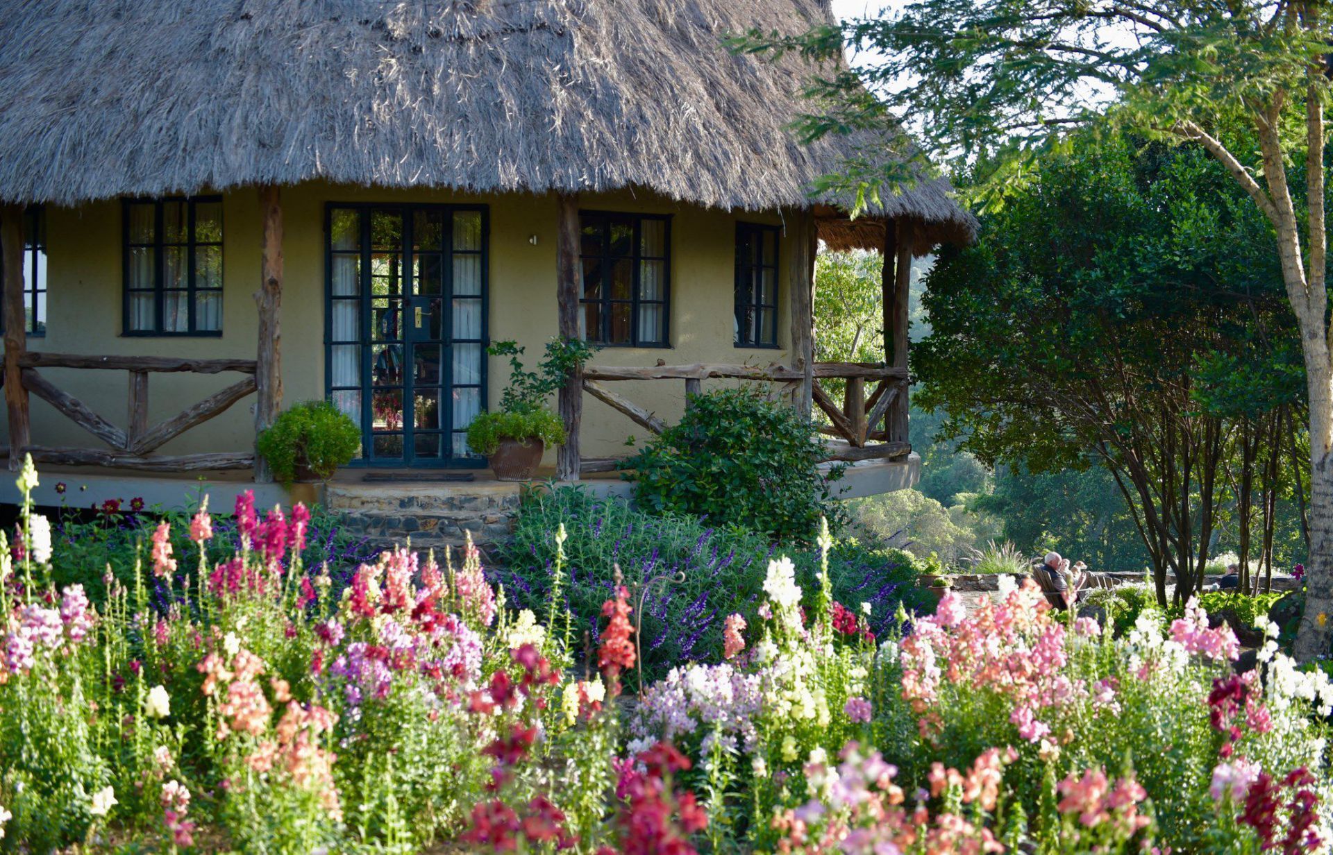 Thatched cottage behind a colorful flower garden and trees