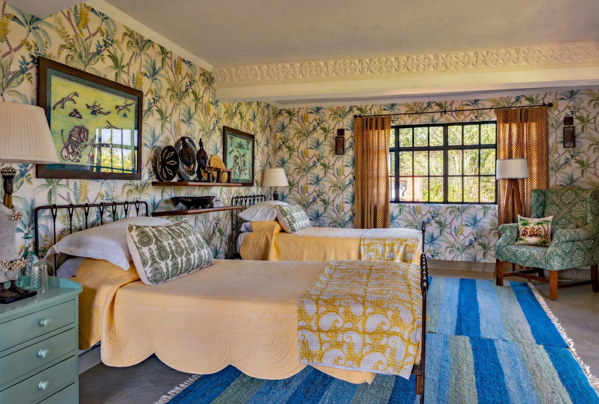 Floral bedroom with twin beds, blue striped rug, and a window with patterned curtains
