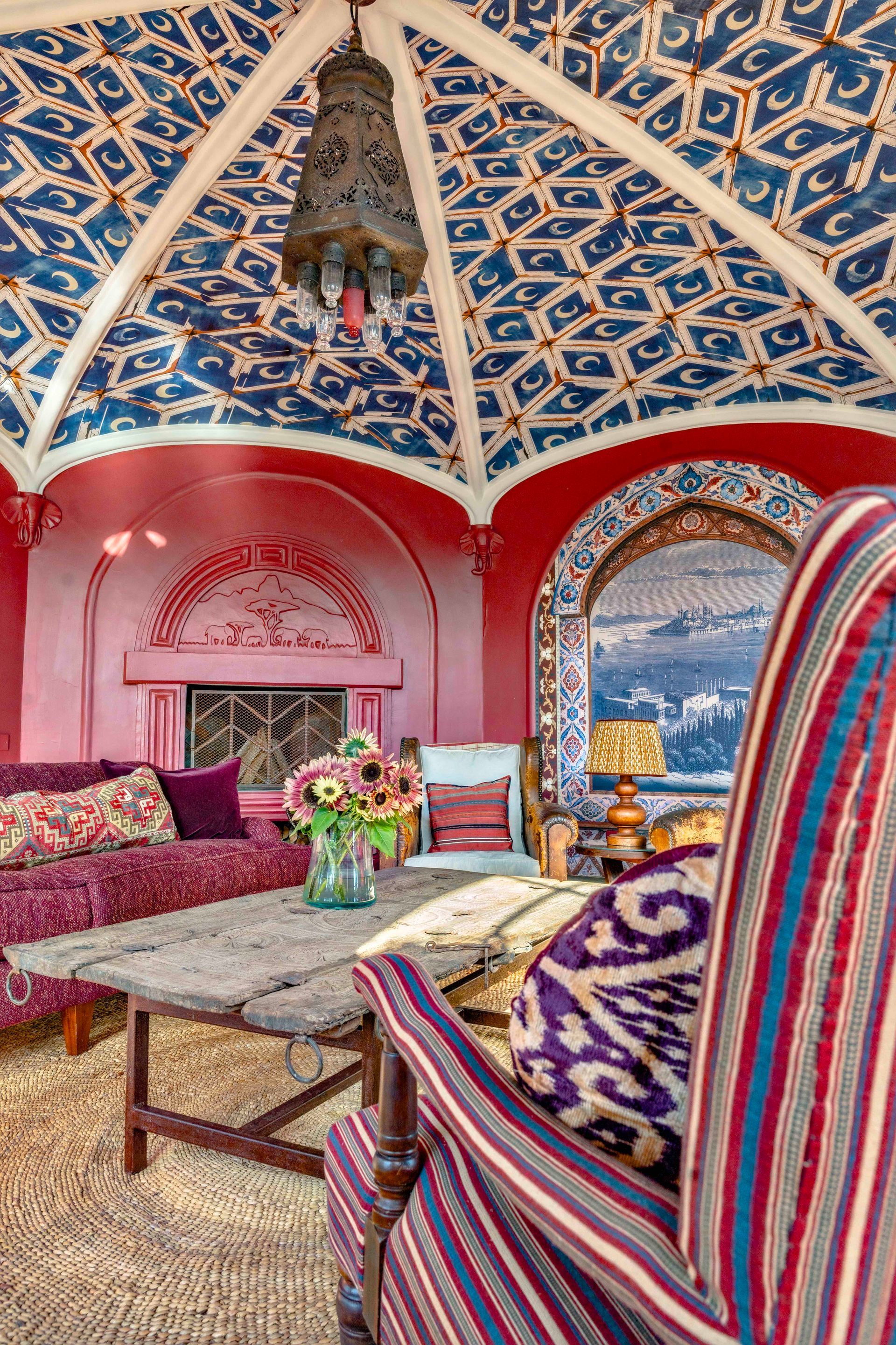 Vibrant red-and-blue living room with ornate painted ceiling, striped chairs, and a sea view through arched windows