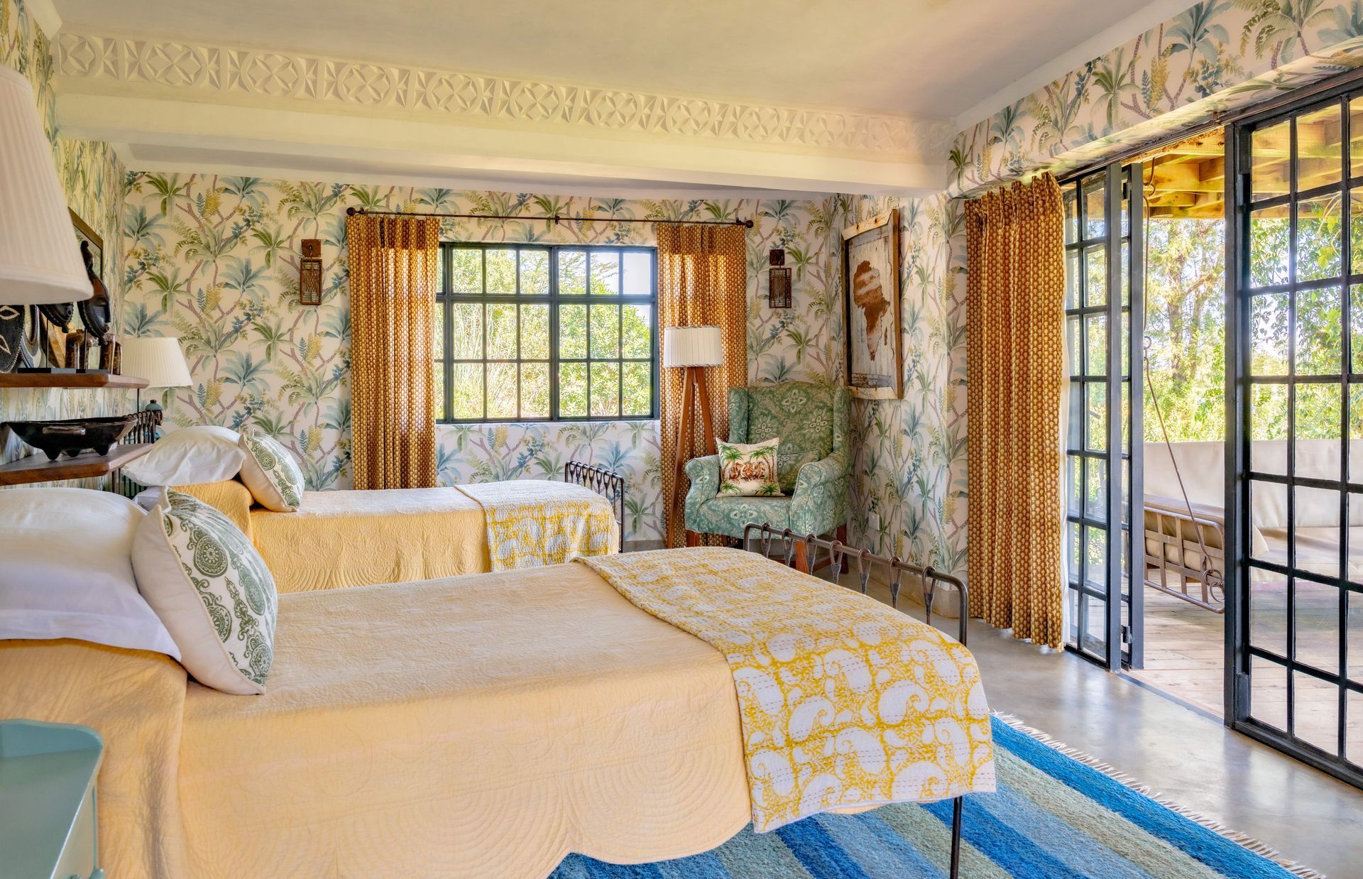 Bright bedroom with two beds, floral curtains, and French doors opening to a balcony.