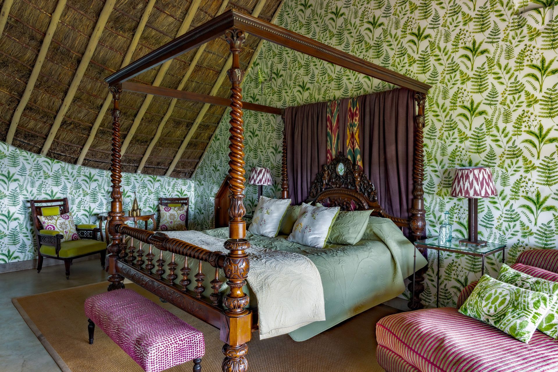 Luxurious canopy bed in a tropical bedroom with floral upholstery, green bedding, and pink benches